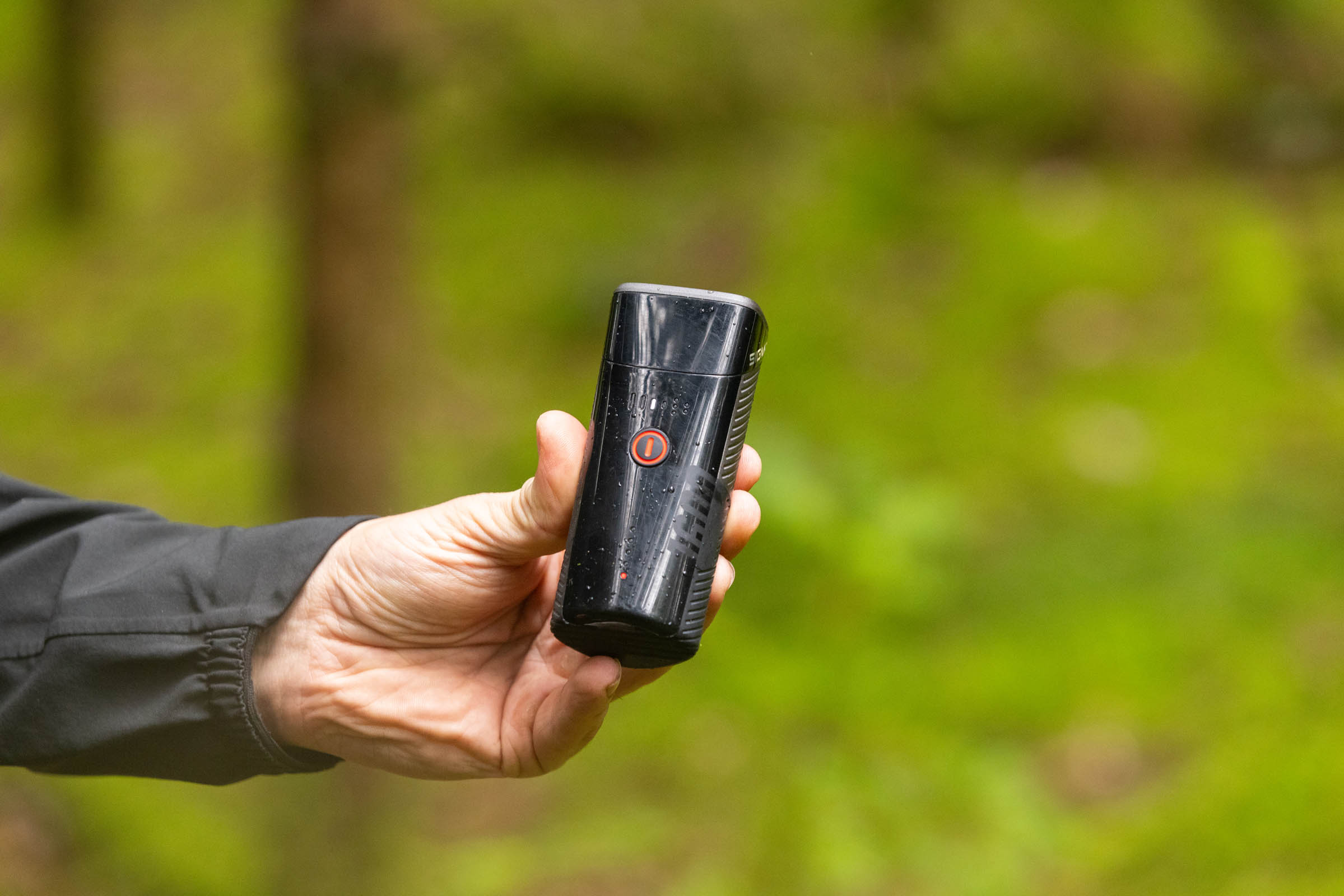 Sigma Buster 1600 front light held in a hand with its illuminated control button and battery indicator visible.
