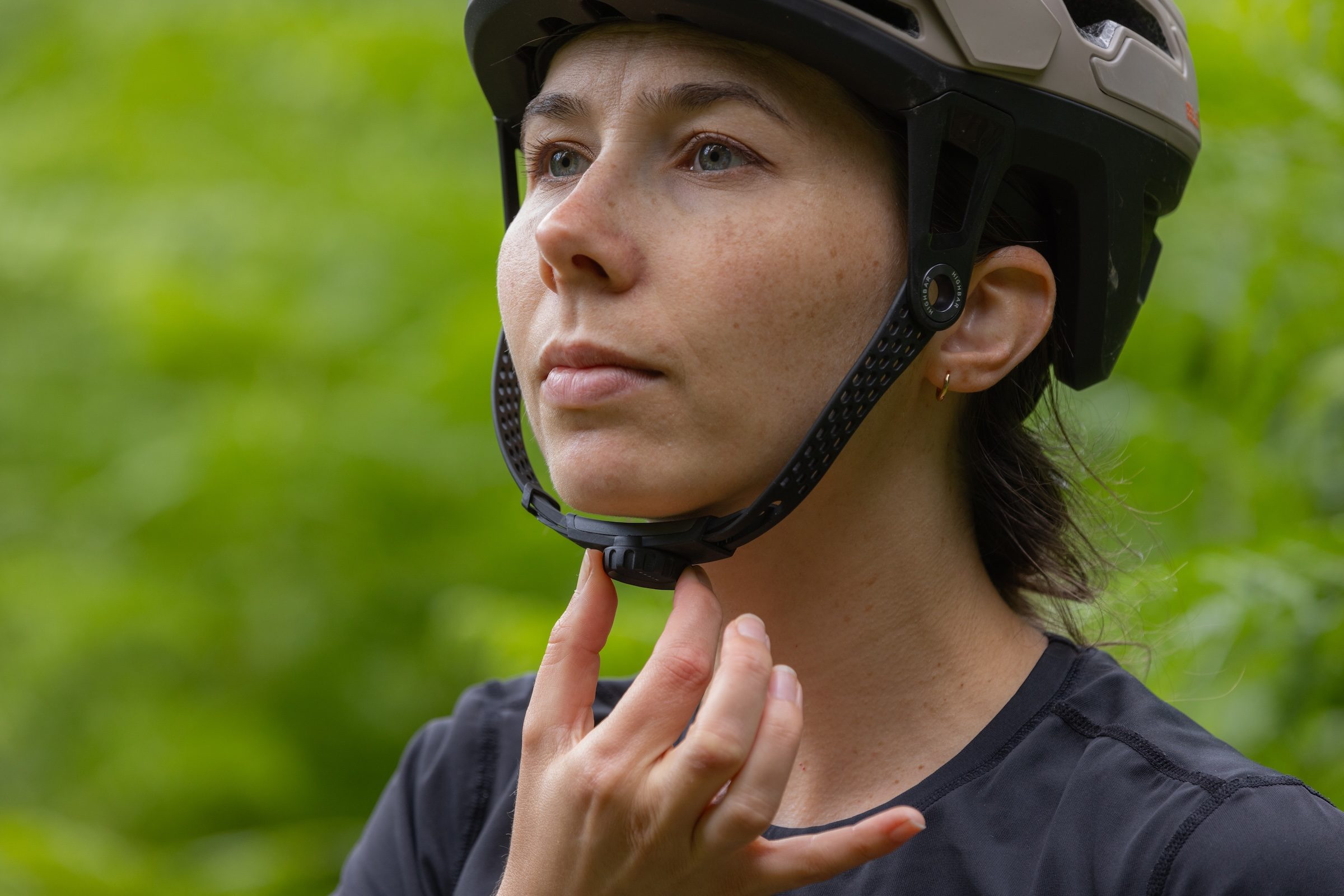 Close-up of a rider adjusting the Canyon Deflectr helmet's HighBar 1.5 chin strap system.