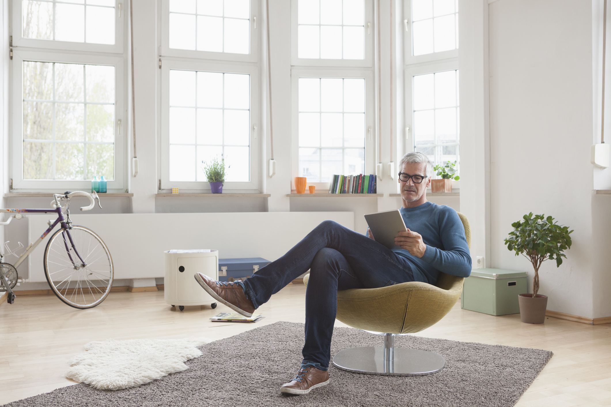 Mature man at home sitting in chair using digital tablet Mature man at home sitting in chair using digital tablet