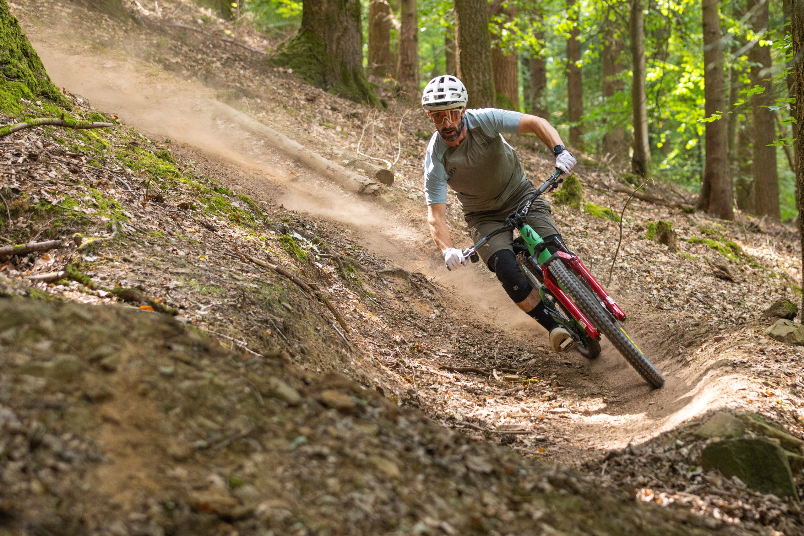 Mountain biker descending through woodland and turning through a dusty corner on a green Specialized Stumpjumper 15 Expert.