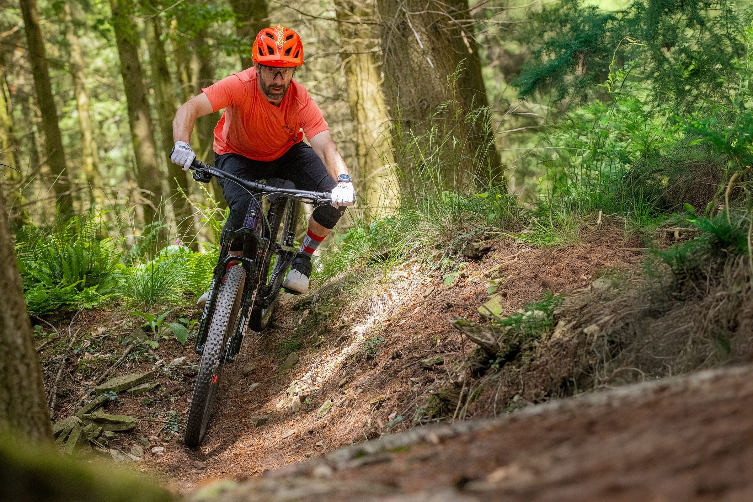 Rider in red jersey, red helmet and black shorts tipping the Santa Cruz Tallboy into a sweeping undulation on the trail.