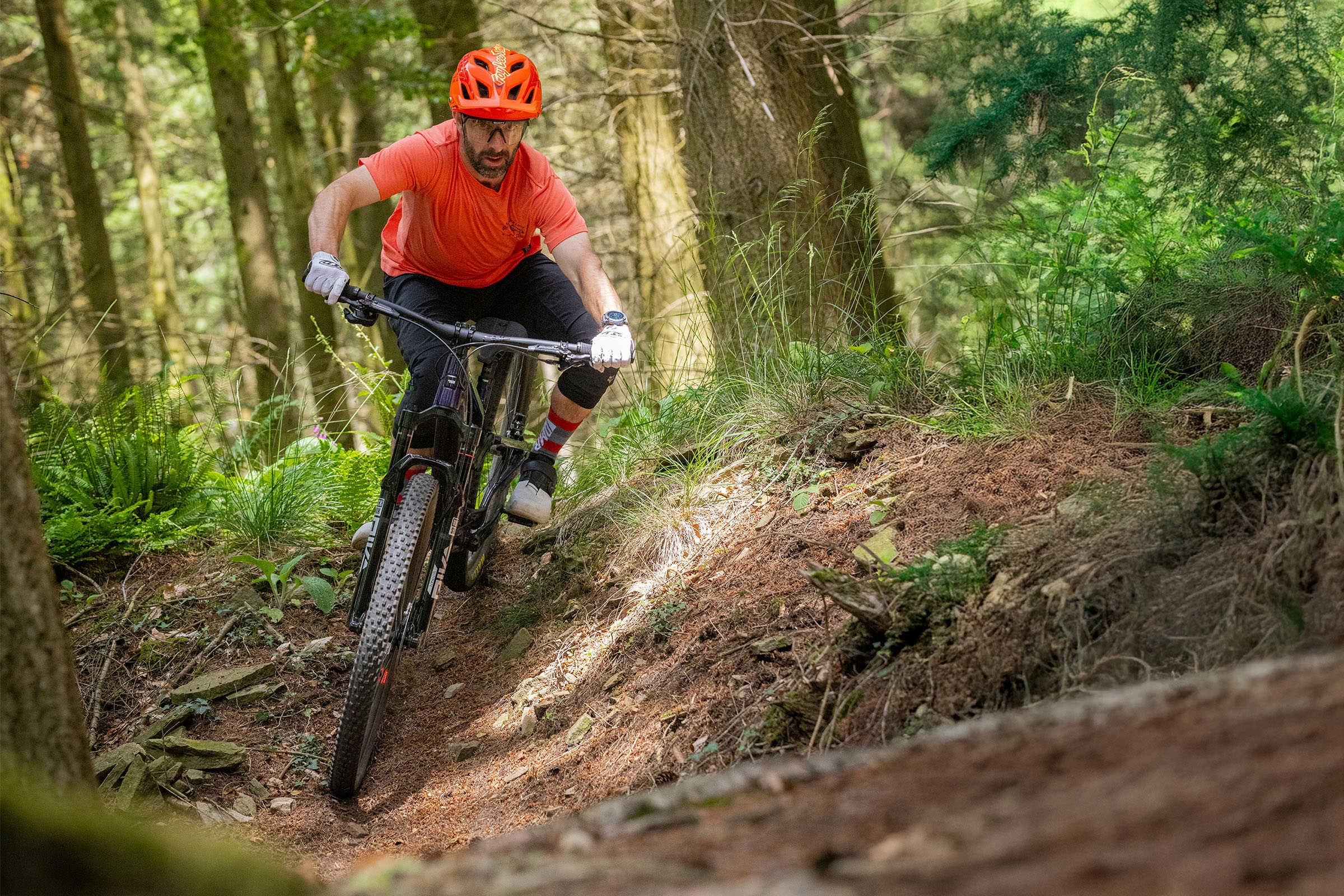 Rider in red jersey, red helmet and black shorts tipping the Santa Cruz Tallboy into a sweeping undulation on the trail.