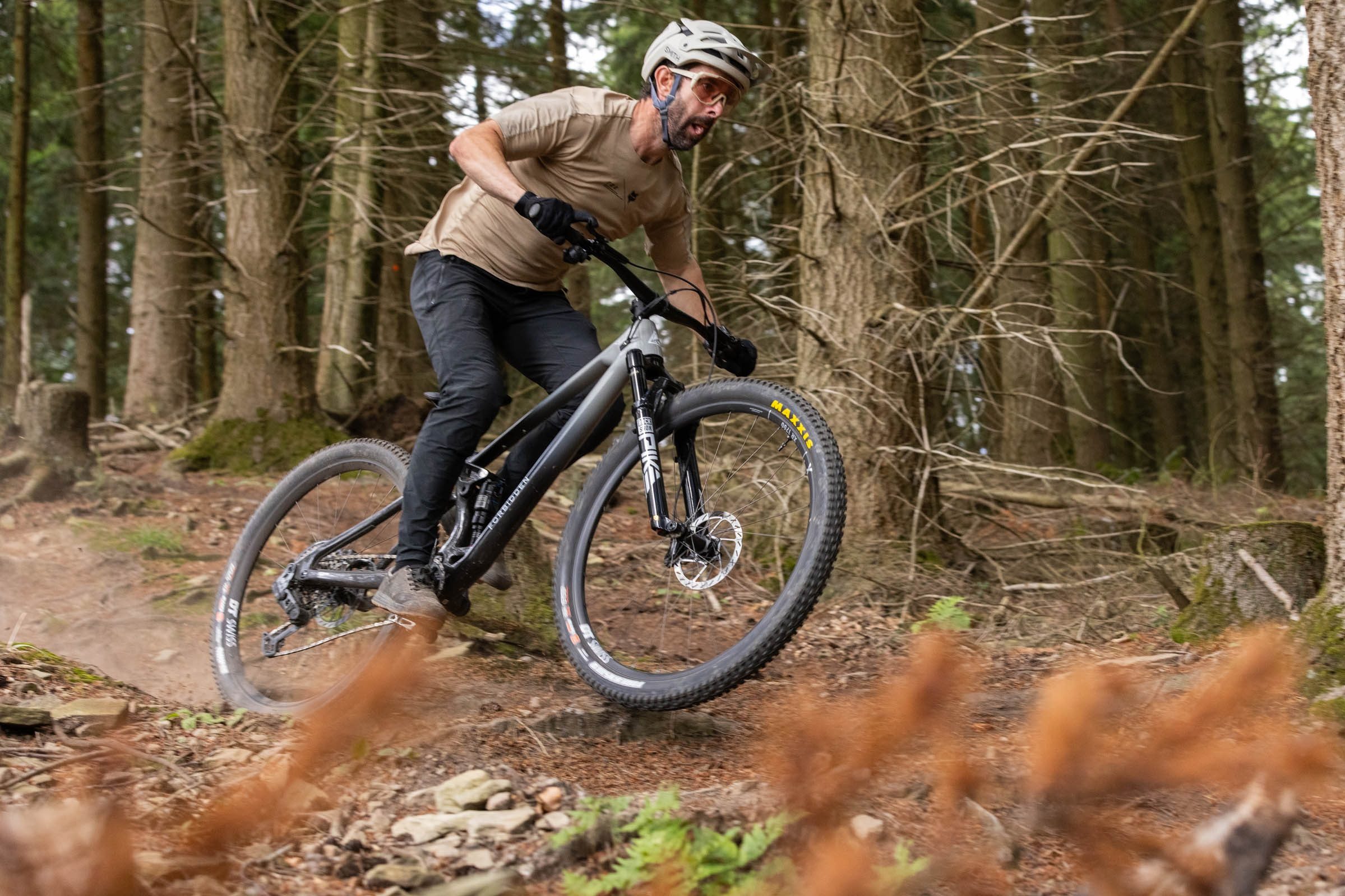 Rider in sandy coloured jersey and helmet with black trousers skipping over roots on a Forbidden Reya.