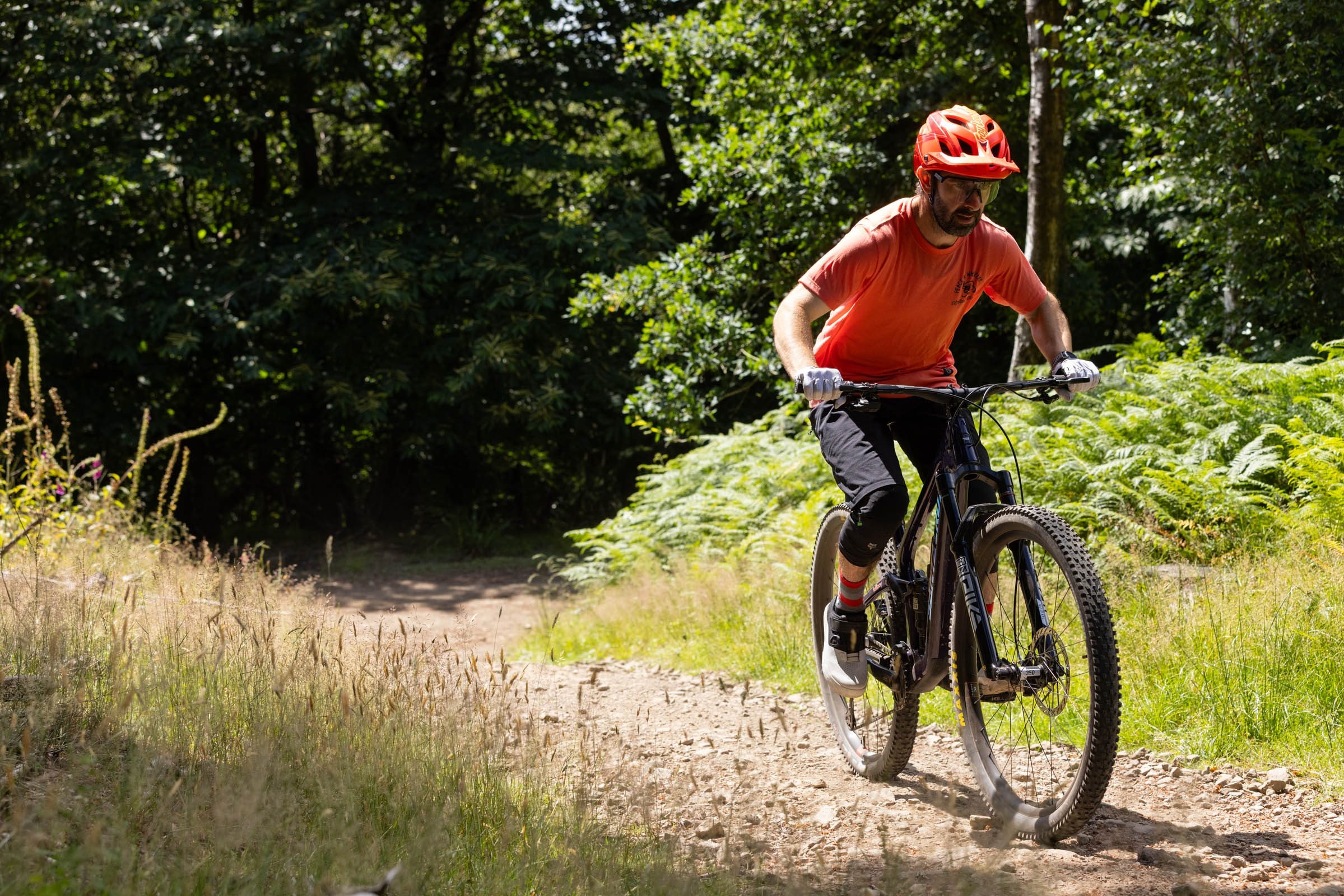 Rider with red jersey, red helmet, black shorts and knee pads climbing on the Santa Cruz Tallboy.
