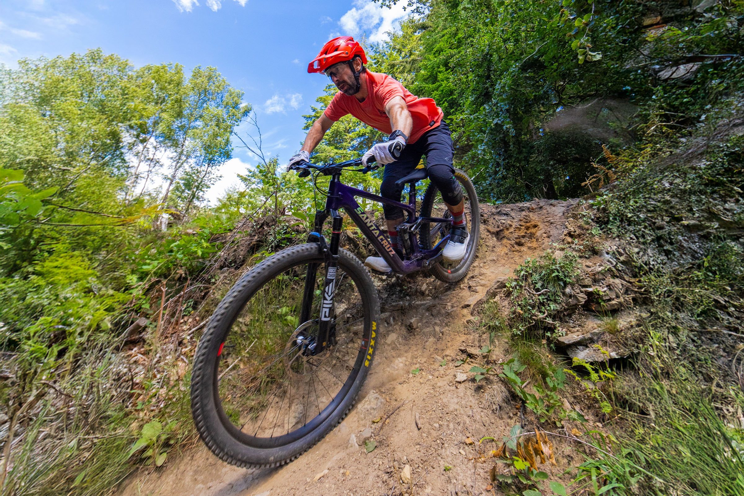Rider in red jersey, red helmet and black shorts dropping into a steep, dusty chute aboard the Santa Cruz Tallboy.