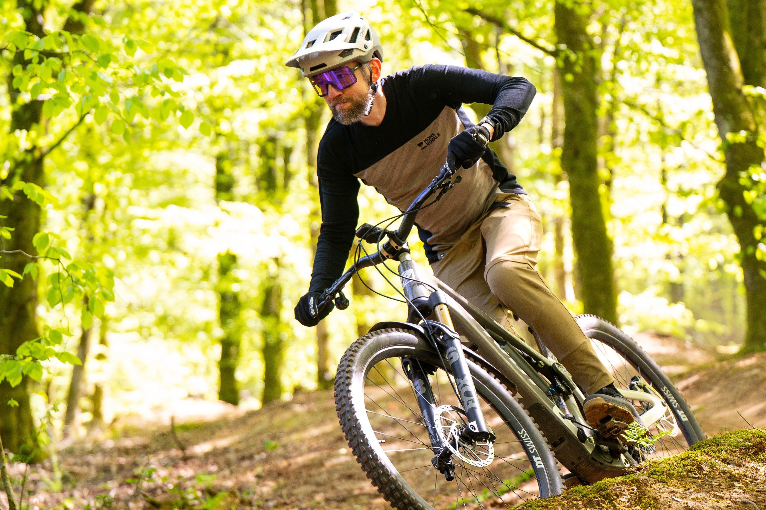 Rider cornering on singletrack cut through a wooded area.