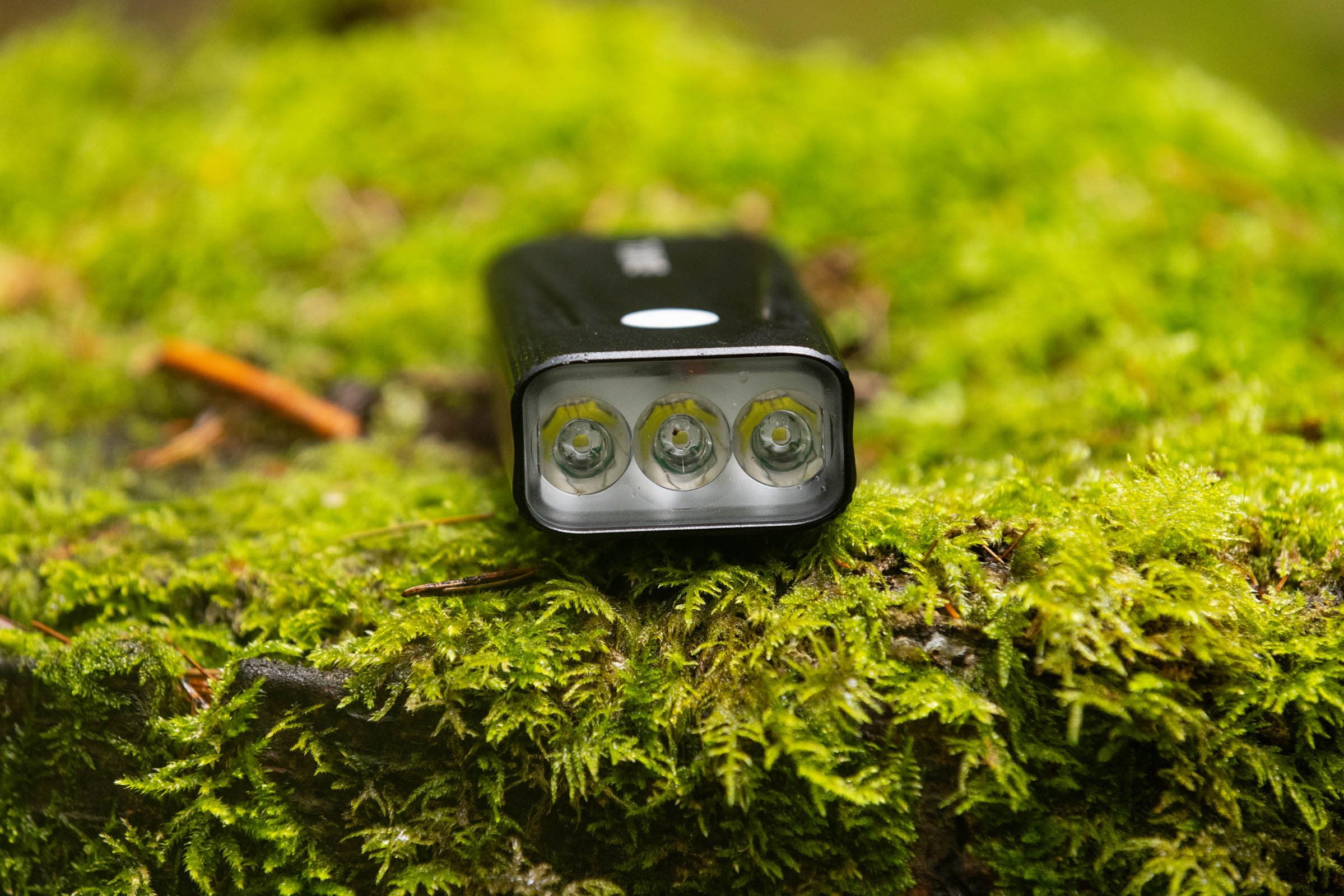Front view of a Bikil 2400 mountain bike light showing its three LED lenses while resting on moss.