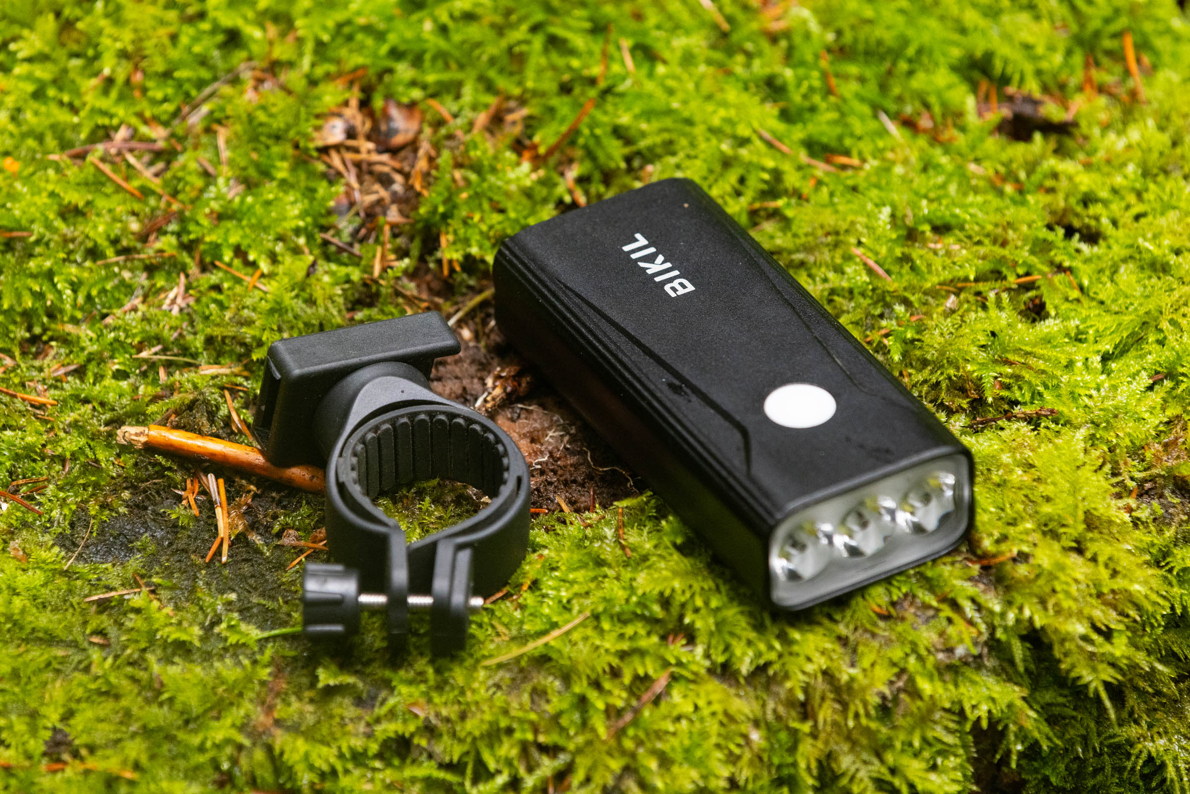 Bikil 2400 mountain bike front light and black handlebar mount resting on moss.