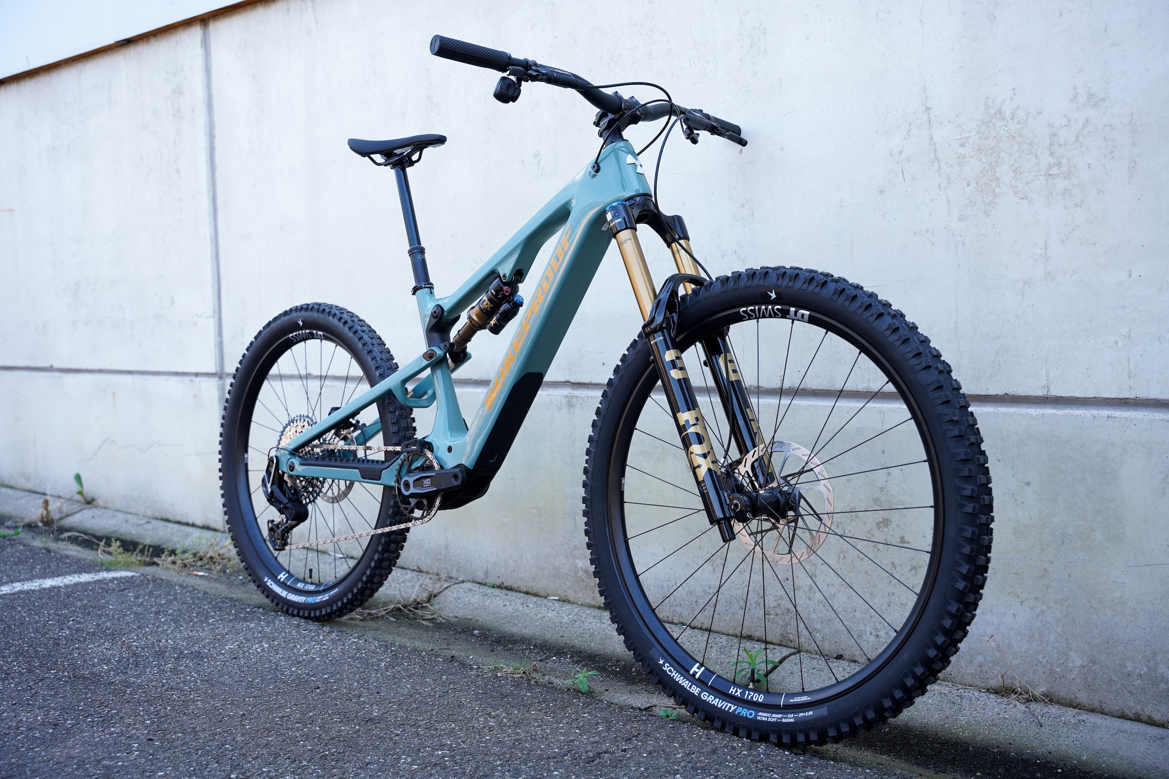 Blue Nukeproof Kilowatt Carbon Factory electric mountain bike photographed from the front three-quarter angle against a concrete wall.