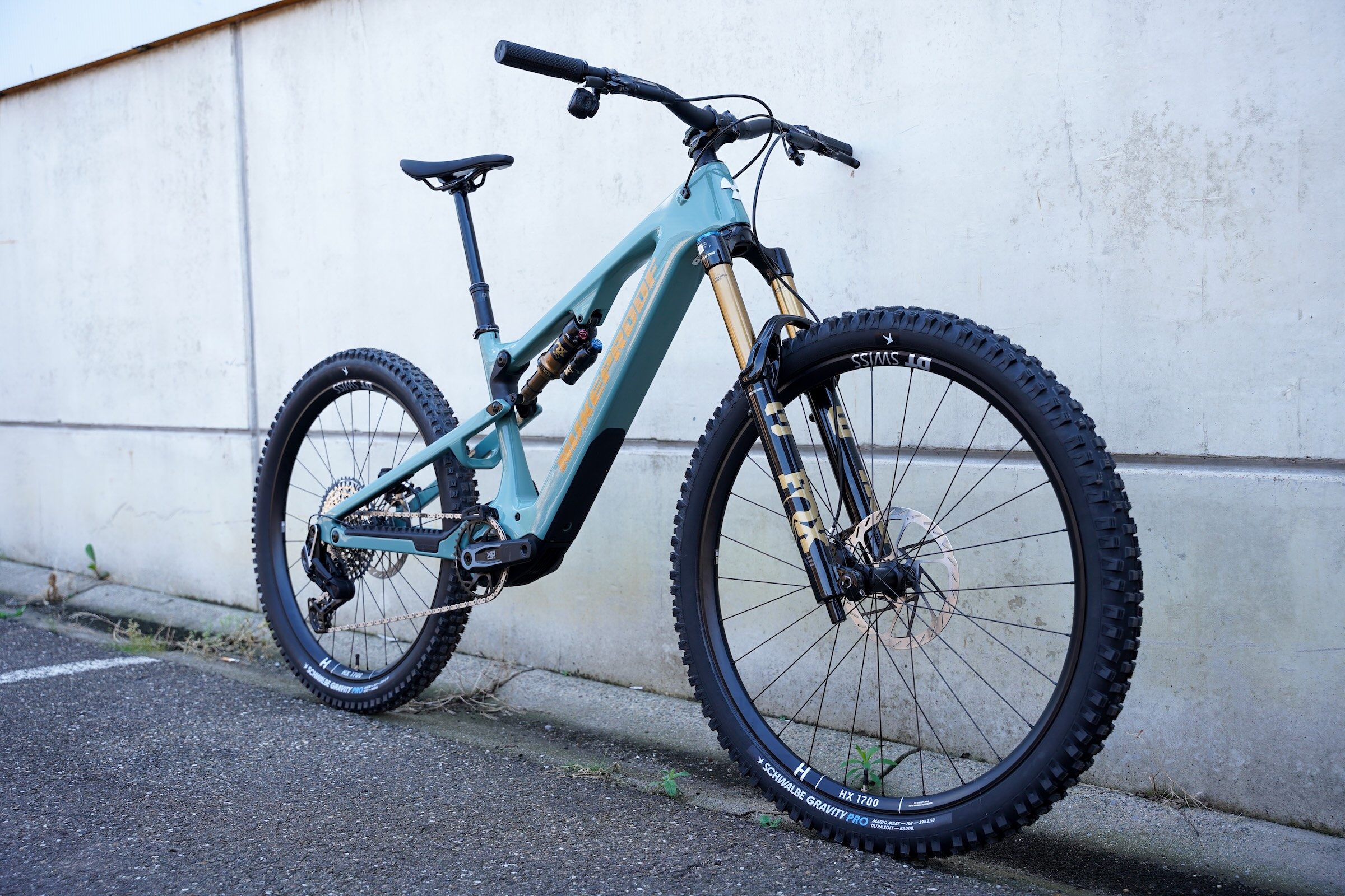 Blue Nukeproof Kilowatt Carbon Factory electric mountain bike photographed from the front three-quarter angle against a concrete wall.
