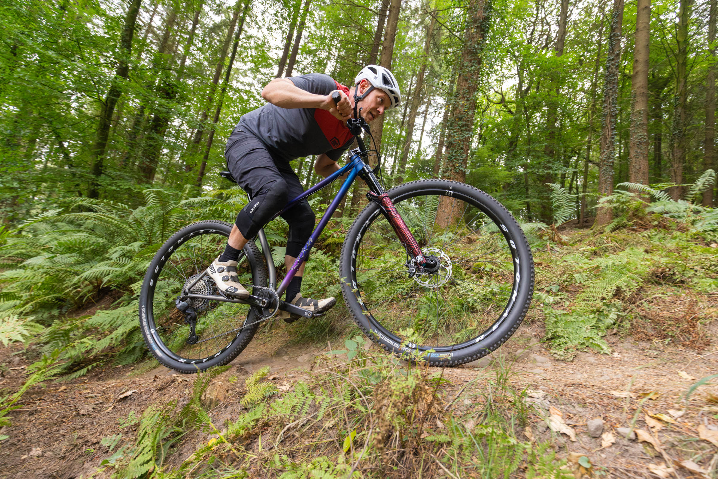 Rider weighting the front wheel of the Sour Cycles Pasta Party 32 over a trail feature in woodland.