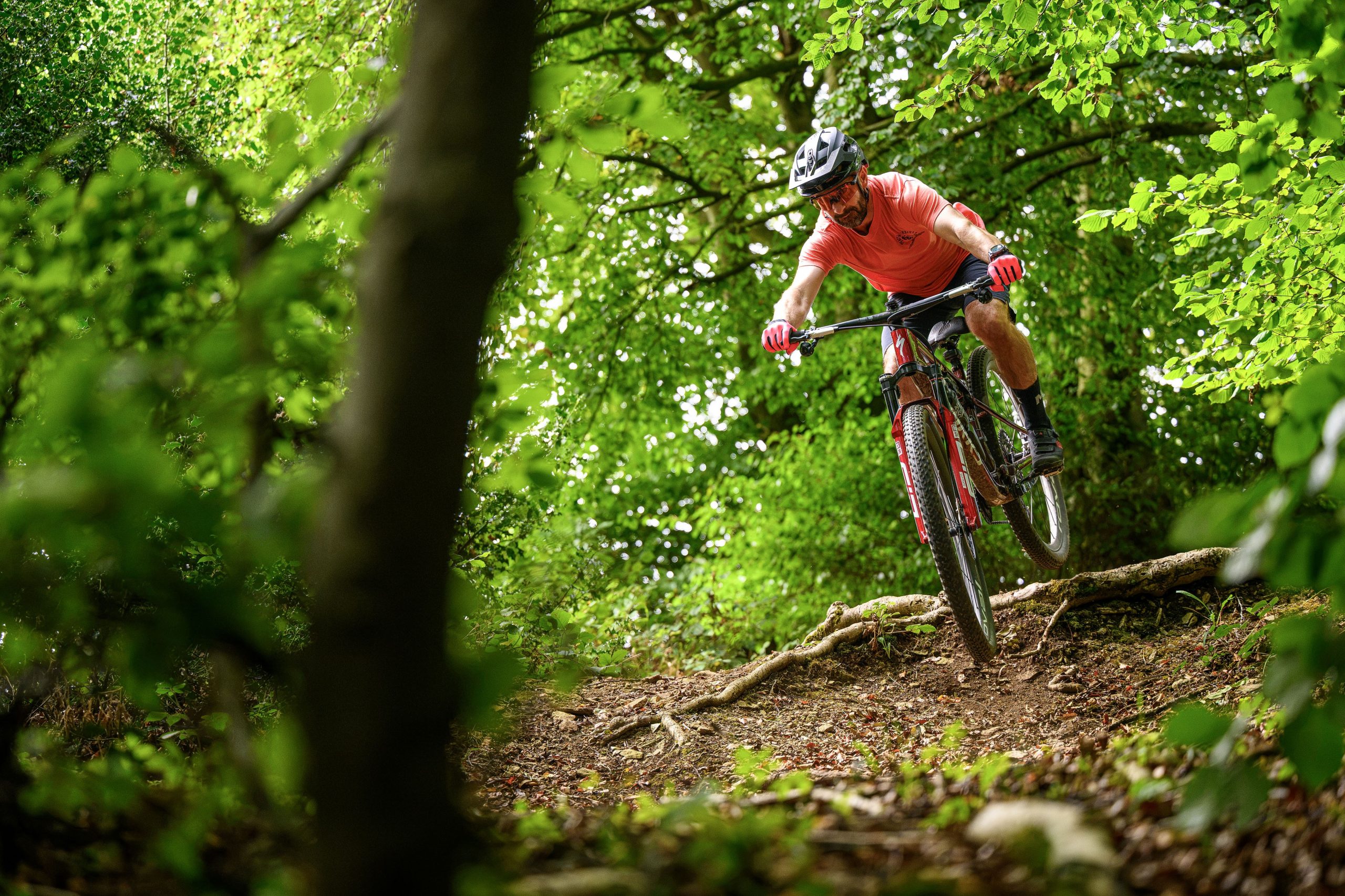 Rider in a red t-shirt dropping over a root step aboard the Specialized Epic 9.