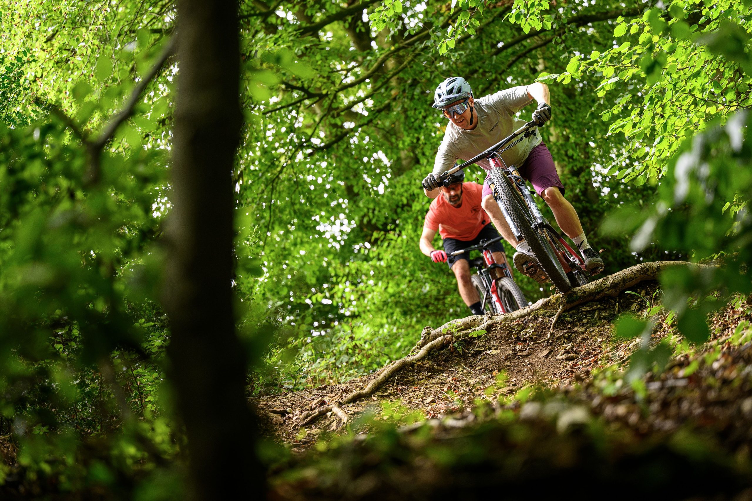 One rider following the other as they drop over a root-step. First rider is on the Orbea Oiz, second is on the Specialized Epic 9.