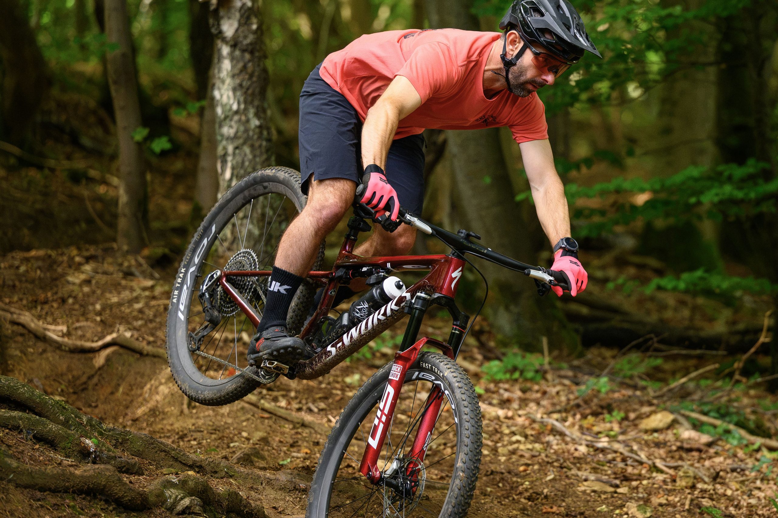Rider in red t-shirt dropping down over a root spread aboard the Specialized S-Works Epic 9.
