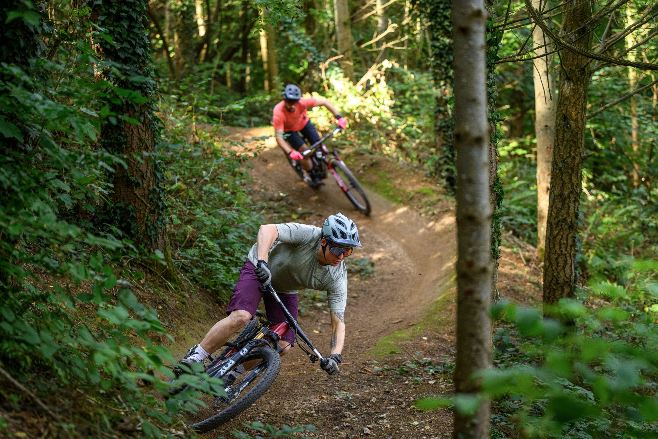 Two riders winding their way through singletrack berms following each other. The first rider is aboard the Orbea Oiz, the second is riding the Specialized Epic 9.