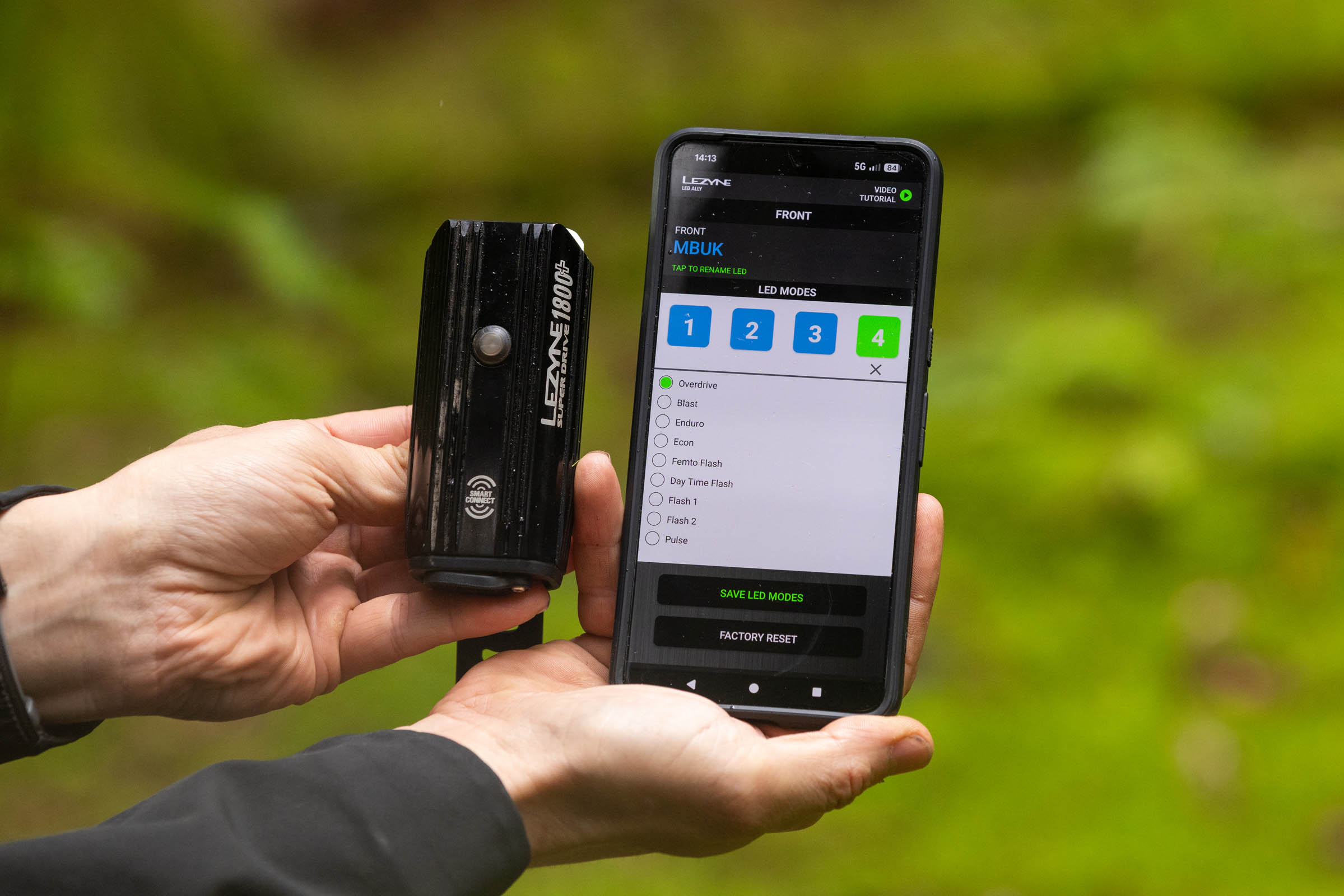 Lezyne Super Drive 1800+ Smart front light beside a smartphone displaying the LED Ally app and selectable light modes.