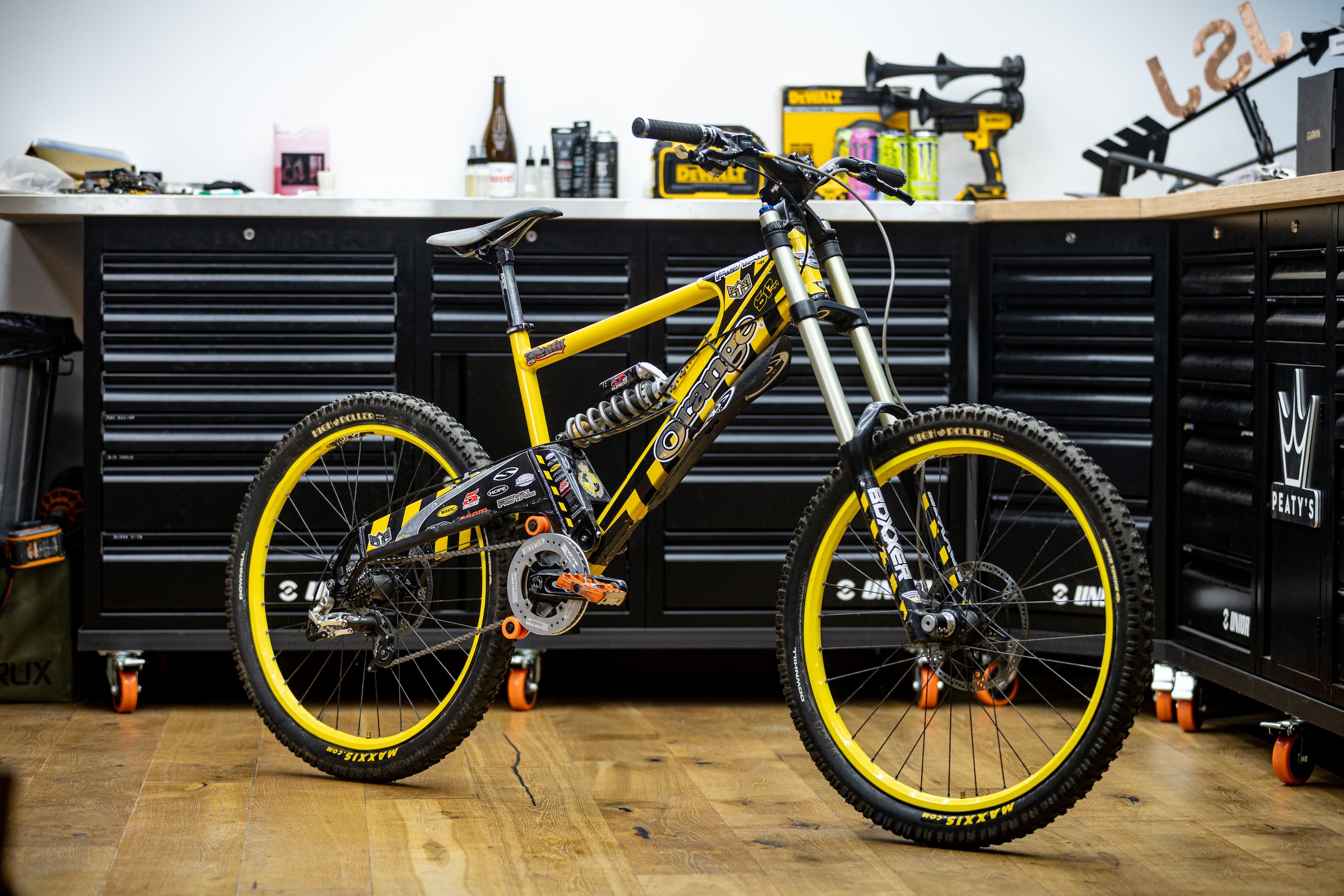 Steve Peat’s yellow and black Orange 224 downhill bike displayed in his workshop, with matching yellow rims and RockShox BoXXer forks.