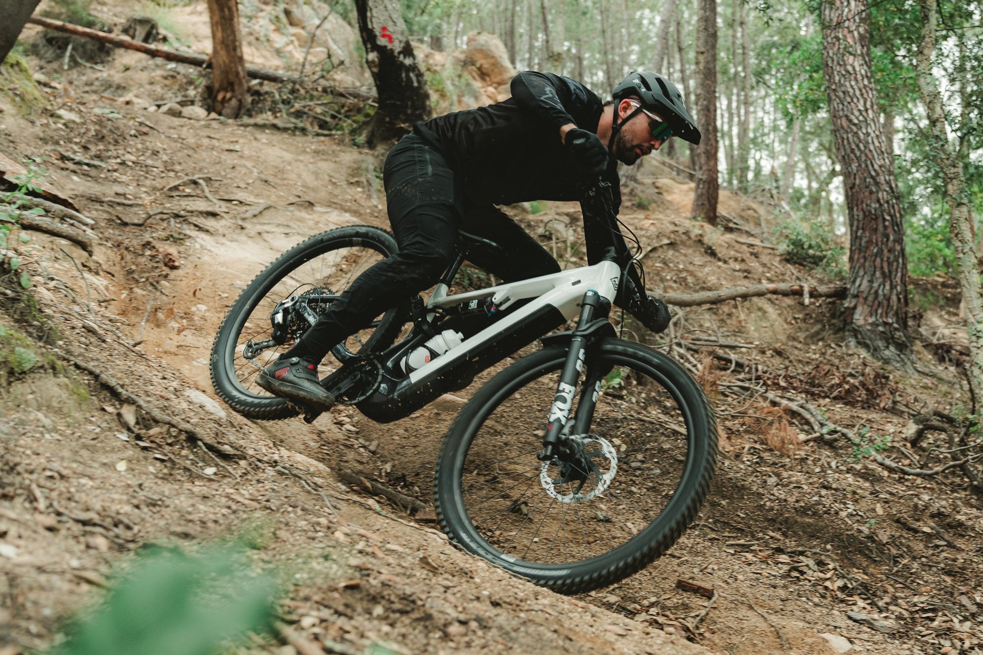 Mountain biker riding through a dry, dusty singletrack turn on a white Megamo Ryal eMTB.