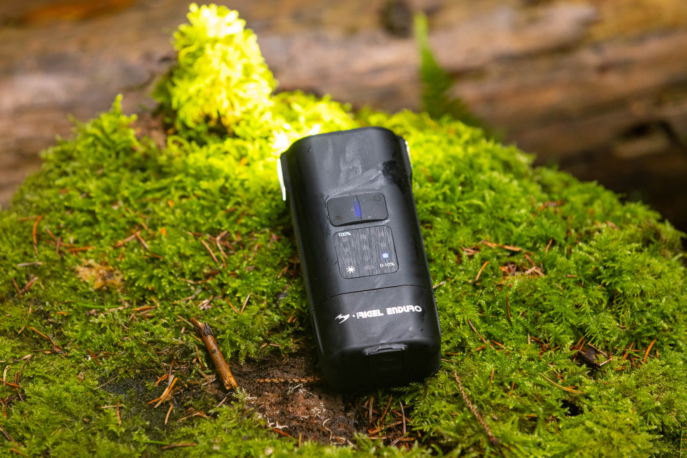 Moon Rigel Enduro 2600 front light showing its top-mounted battery display and control buttons while resting on moss.