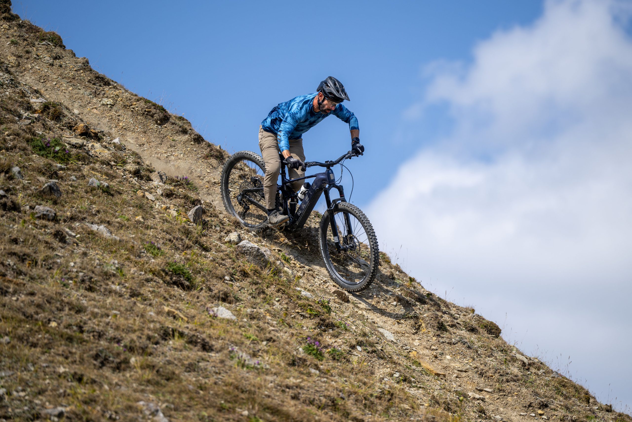Rider descends a steep, rocky hillside on the dark blue Marin Alpine Trail E XR eMTB