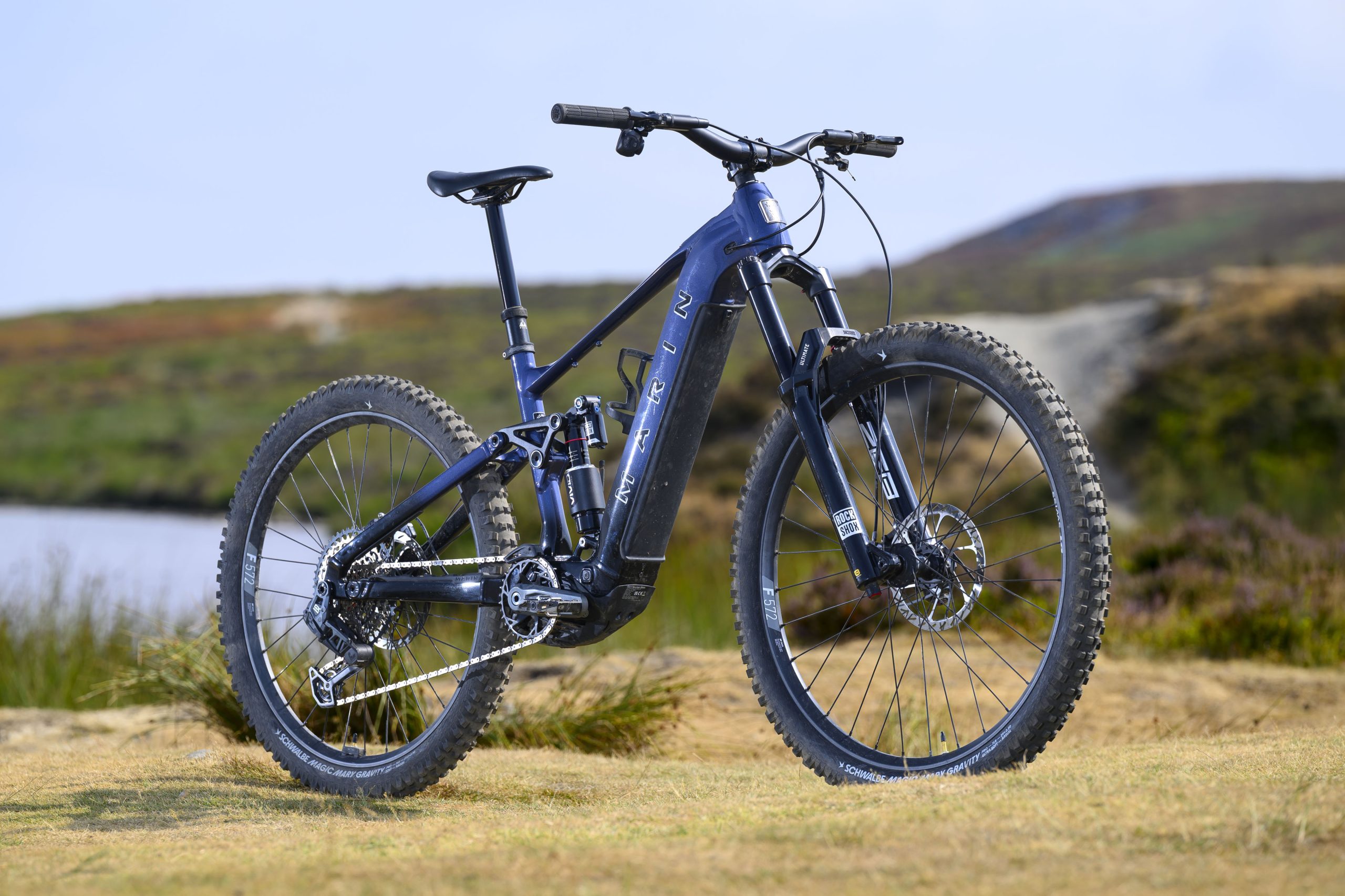 Dark blue Marin Alpine Trail E XR electric mountain bike shown from the front three-quarter angle with mixed wheels and RockShox suspension