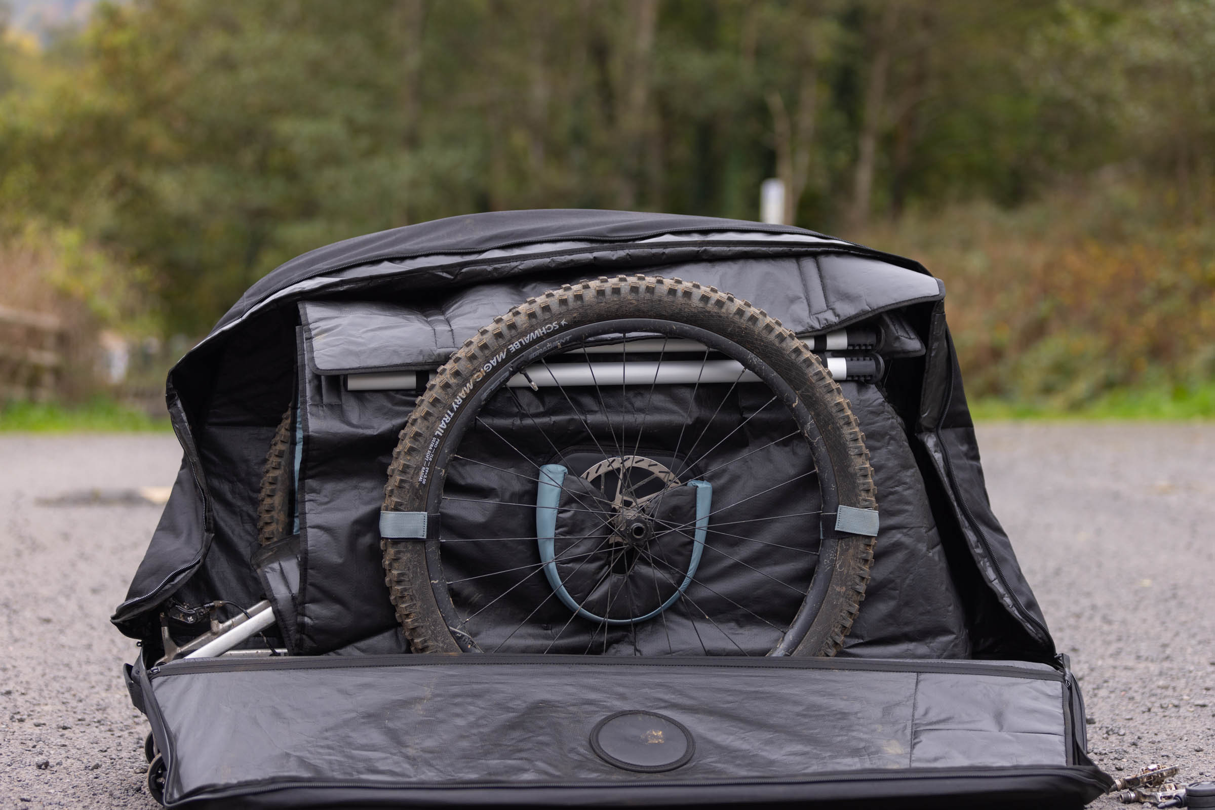 Mountain bike wheel secured with Velcro straps inside an open Thule RoundTrip MTB travel case, with a protective cup covering the brake rotor.