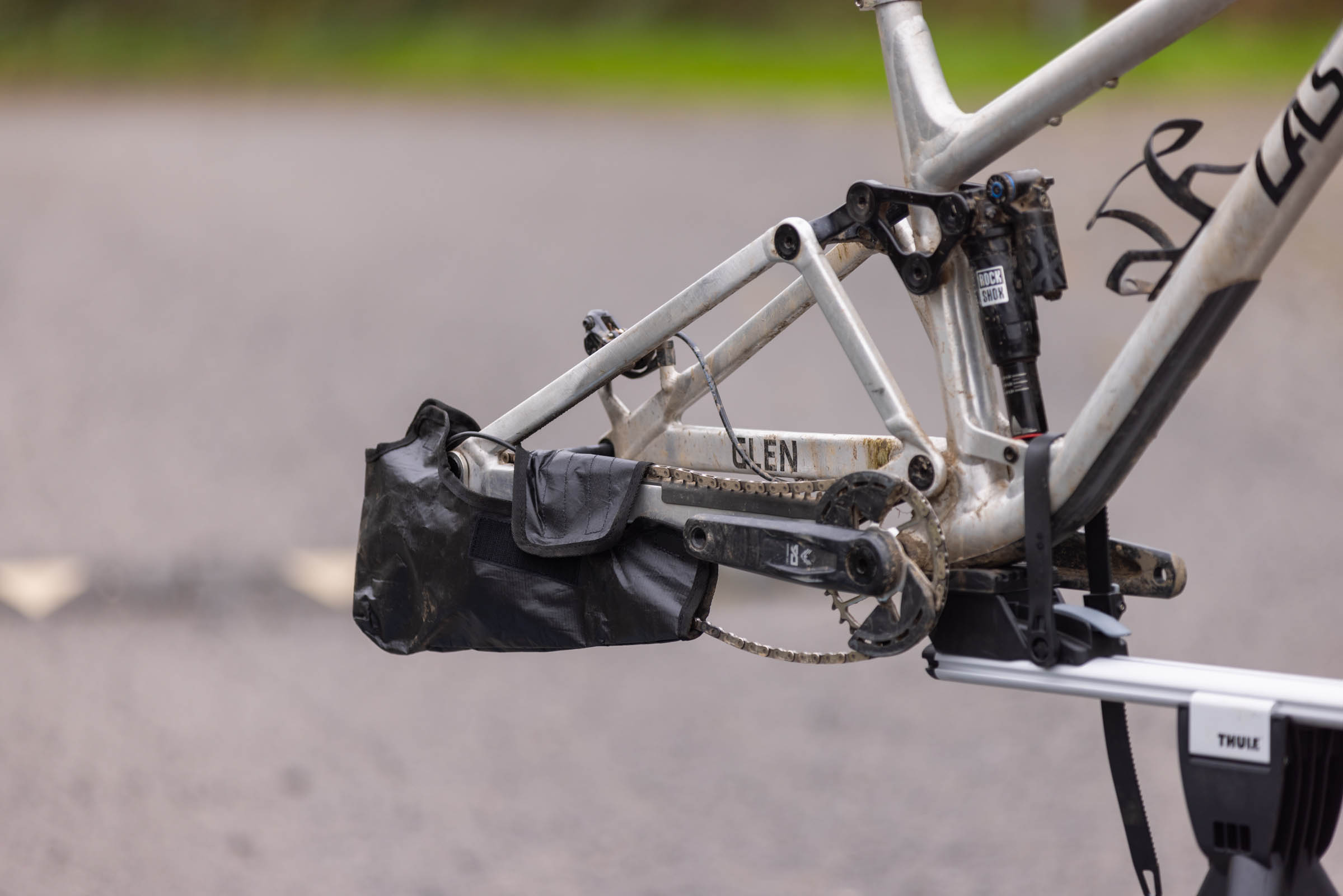Close-up of a silver Last mountain bike with its rear wheel removed and a black protective sleeve covering the rear derailleur and chain.