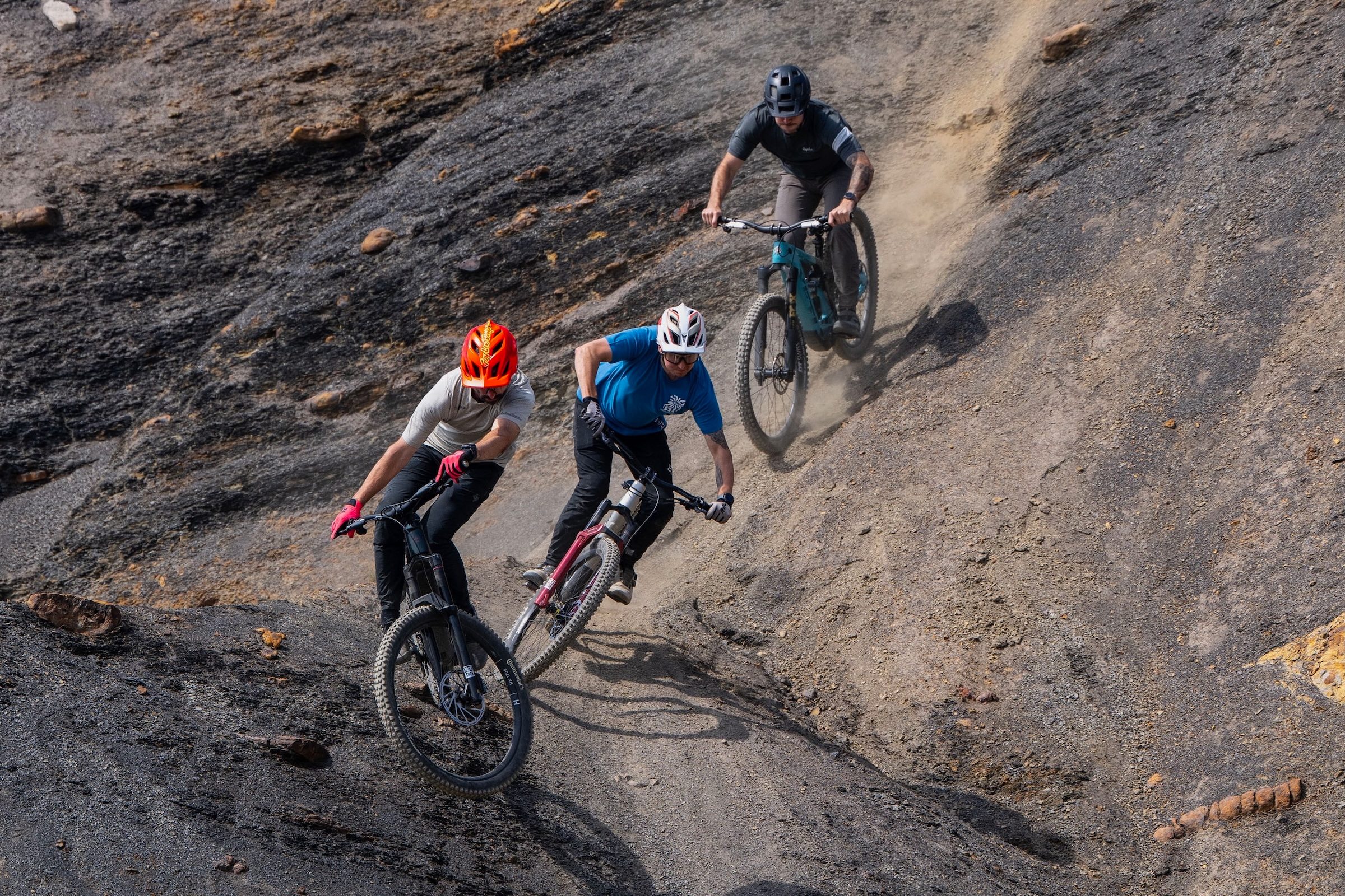 Three riders descending a dusty, rocky trail on full-suspension electric mountain bikes.