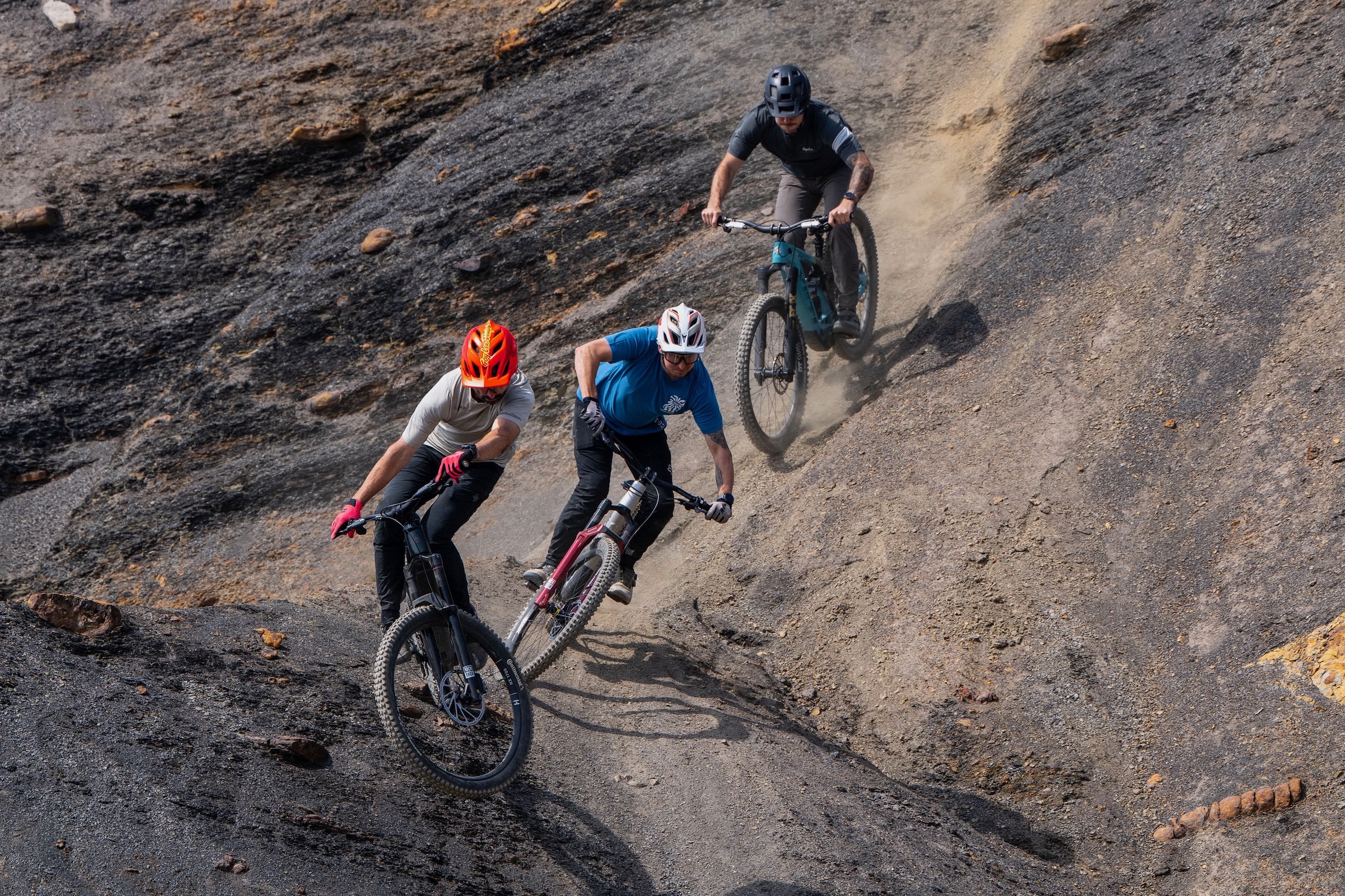 Three riders descending a dusty, rocky trail on full-suspension electric mountain bikes.
