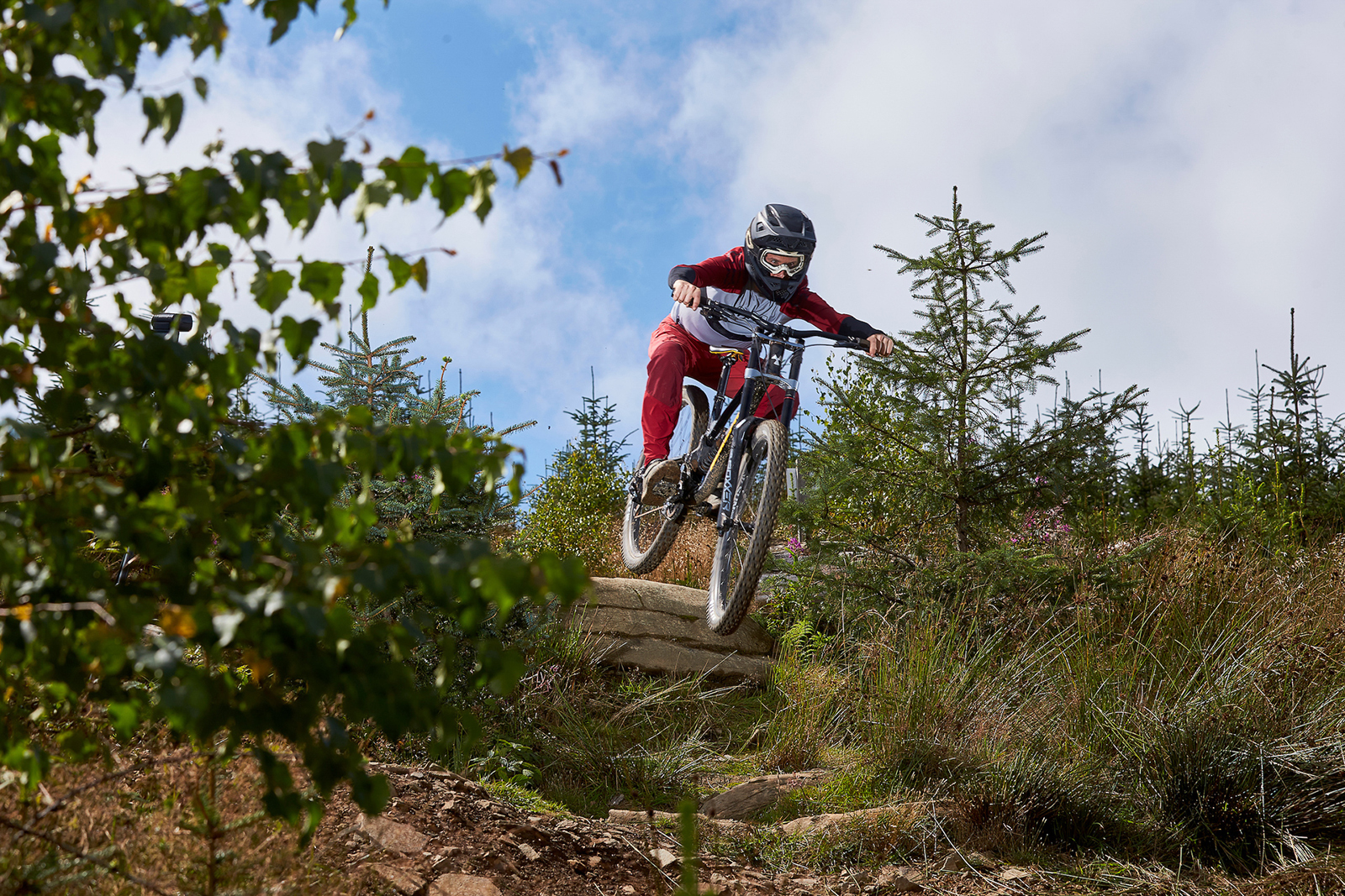 male cyclist wearing red riding black full suspension mountain bike on dirt track