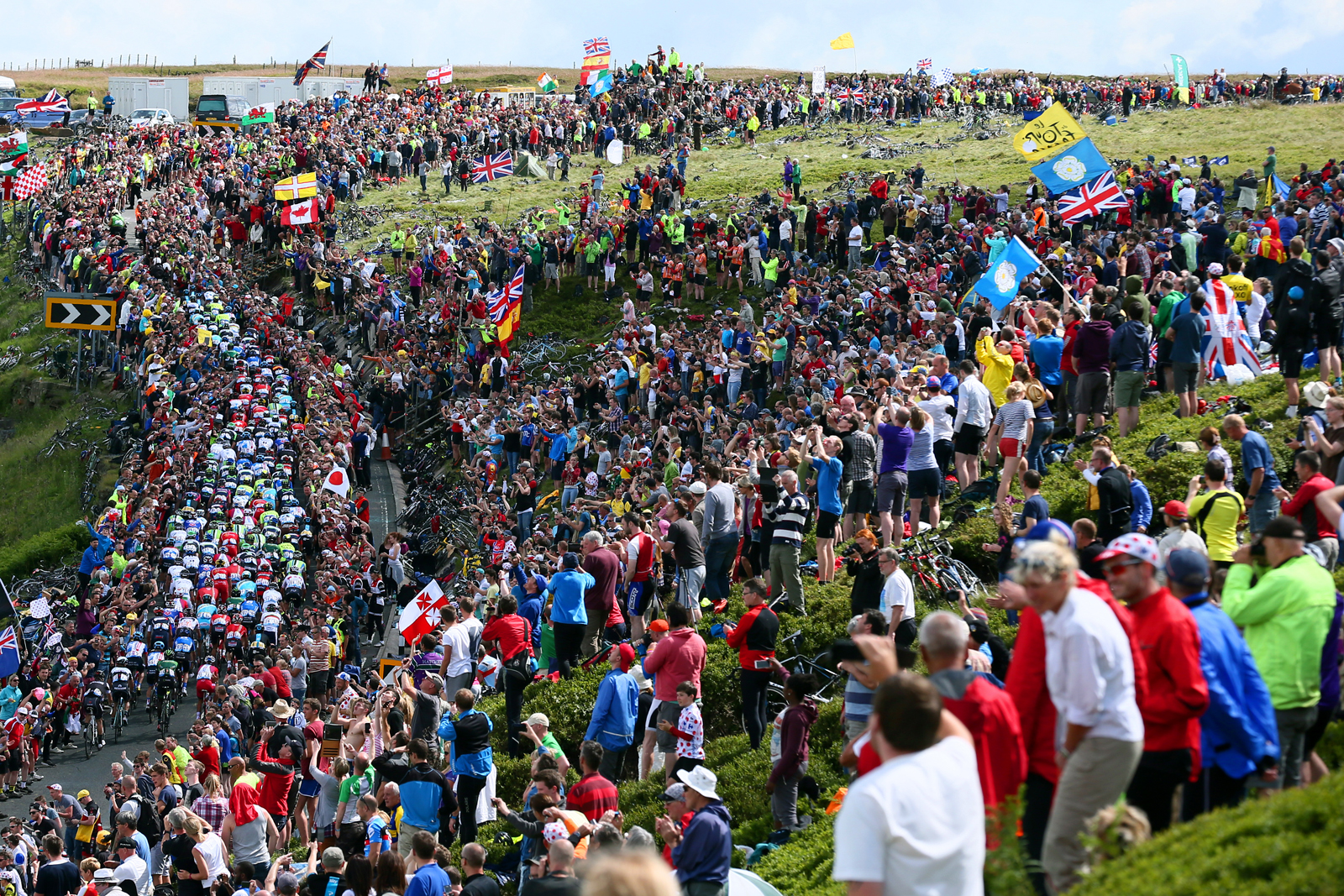 Crowd at Tour de France in Yorkshire as peloton cycles up climb.