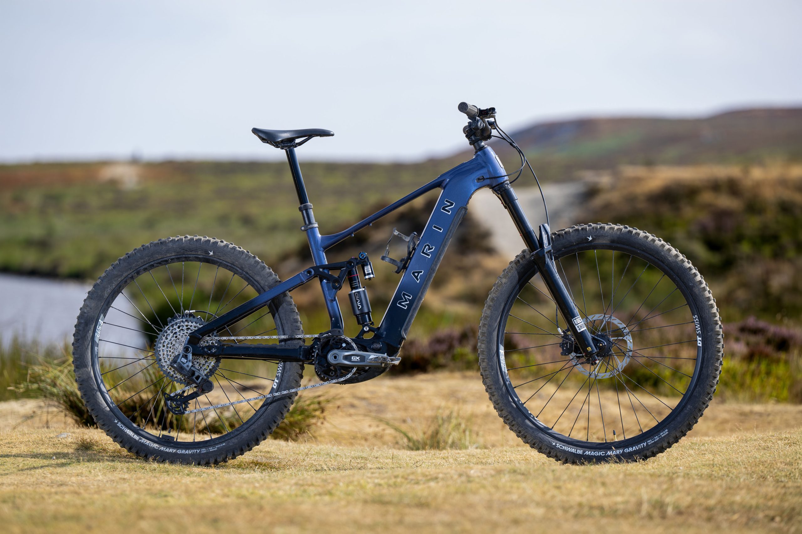 Dark blue Marin Alpine Trail E XR electric mountain bike shown in side profile with mixed wheels and RockShox suspension
